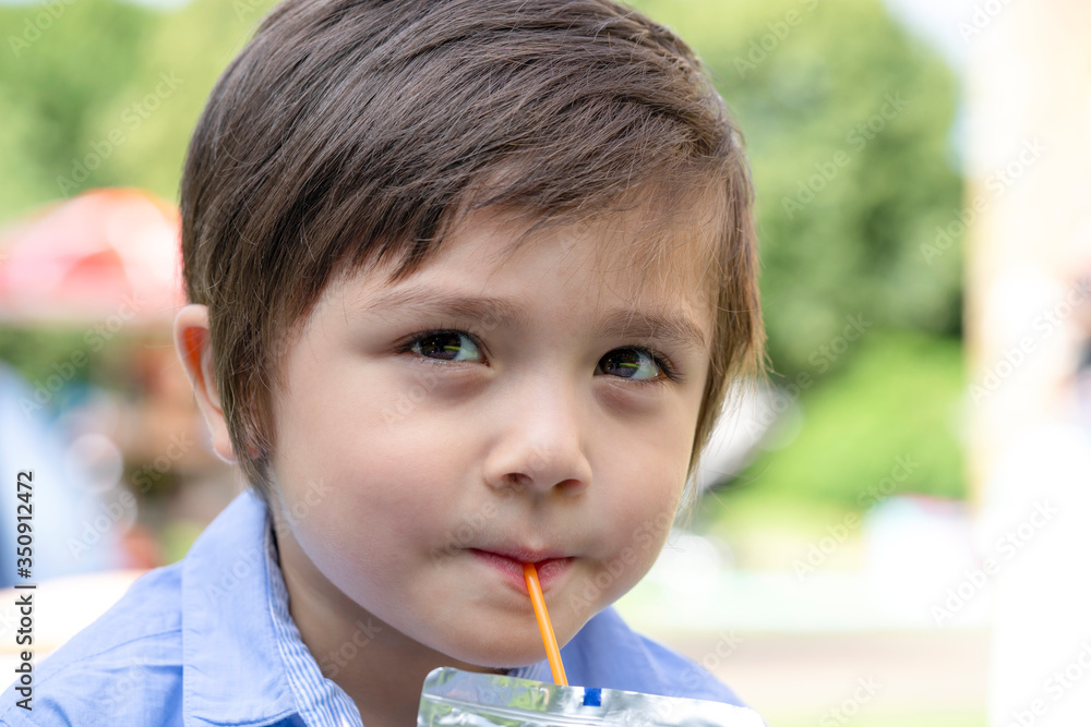 Cute toddler boy with smiling face drinking cold drink with blurry nature on summer,Candid shot Happy Child sitting outside in the park drinking soda or soft drink with a straw,Unhealthy drink for kid Cute toddler boy with smiling face drinking cold drink with blurry nature on summer,Candid shot Happy Child sitting outside in the park drinking soda or soft drink with a straw,Unhealthy drink for kid