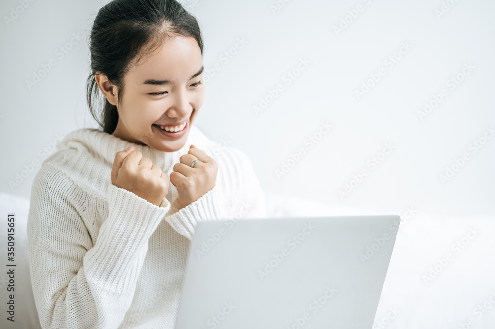 A woman wearing a white shirt on the bed and playing laptop happily. A woman wearing a white shirt on the bed and playing laptop happily.