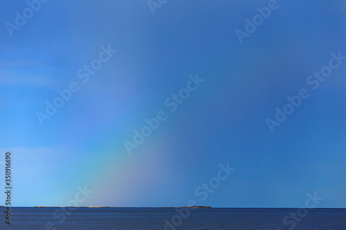 Rainbow in the blue sky with clouds over sea