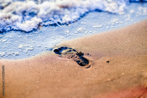 imprint of a foot on a sandy beach near the sea waves at sunset. concept of summer holidays, space for text