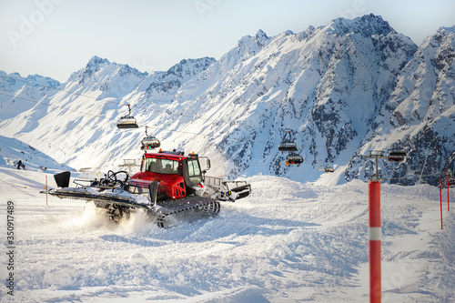 Red modern snowcat ratrack with snowplow snow grooming machine preparing ski slope piste hill at alpine skiing winter resort Ischgl in Austria. Heavy machinery mountain equipment track vehicle photo