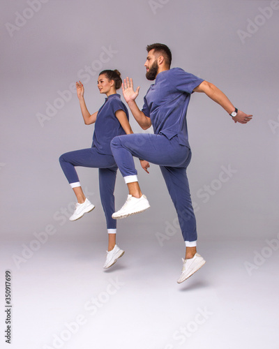 funny relationship. two young stylish happy girl and guy in blue costumes are jumping up together in moment with smile on the gray wall background, lifestyle concept, free space
