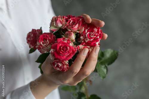 Bouquet of fresh flowers in woman's hand. Female hand holds flowers near the gray wall. Art decoration at the wedding. Florist. Image with selective color.