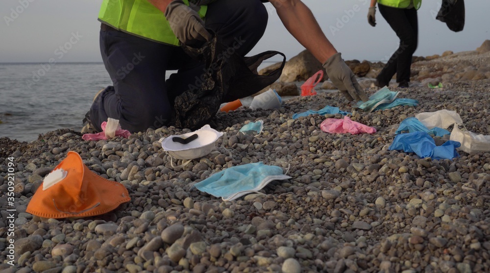 Obraz premium Covid-19 plastic waste. Used disposable medical masks and gloves thrown out by the waves. Volunteers collect garbage on the sea coast. Pollution of the ocean during a pandemic coronavirus