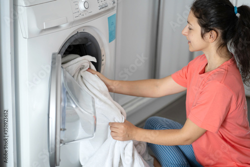 A girl loads dirty laundry into a washing machine while sitting on the floor in an apartment. Laundry day  housework