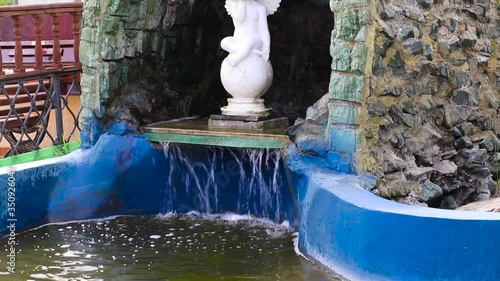 A small waterfall in an artificial grotto in a pond, water falls down, closeup.