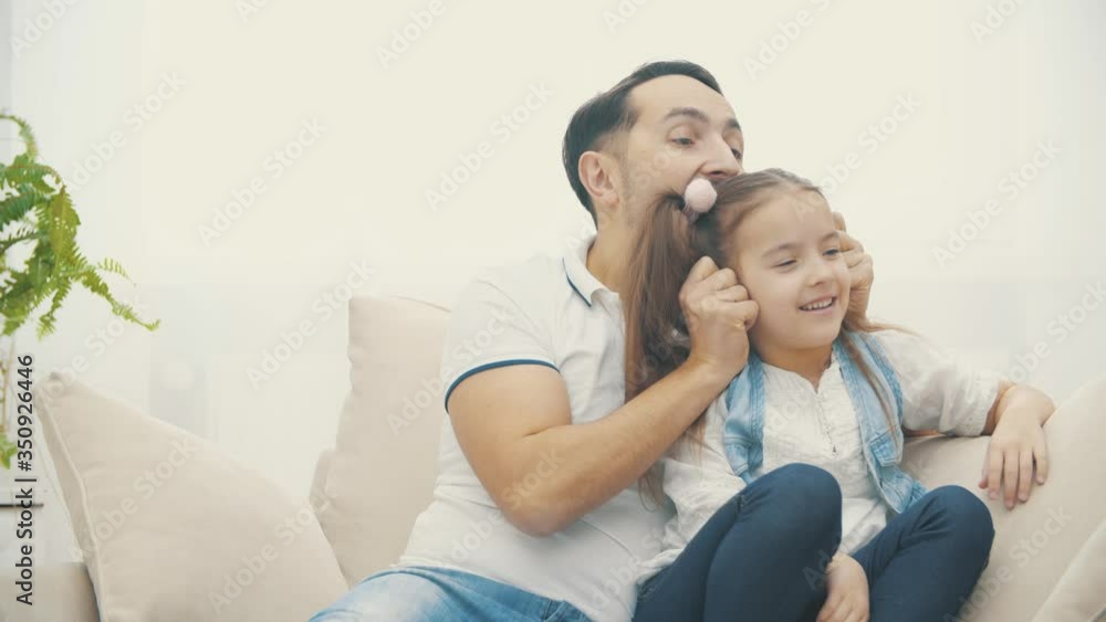 4k video of view where dad touching his daughter hair on a white sofa in the living room. 4k video of view where dad touching his daughter hair on a white sofa in the living room.