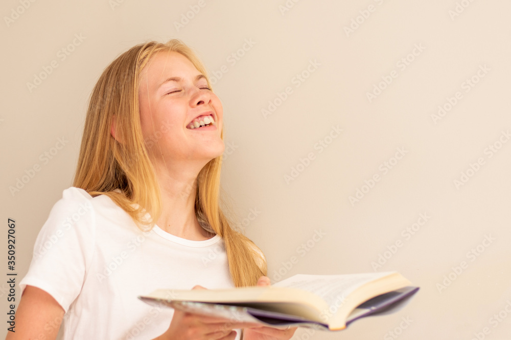 Teenage girl laughing with the book in her hand. Love to read. Selective focus Teenage girl laughing with the book in her hand. Love to read. Selective focus