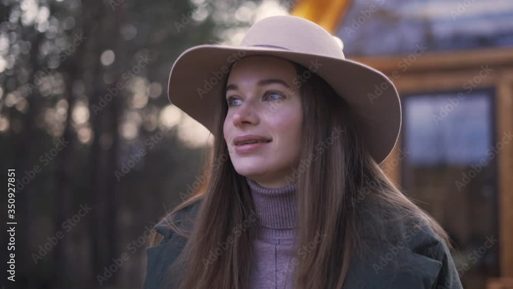 Smiling young woman in a hat against the background of a wooden house with lanterns in the evening. Concept Traveler Enjoys the Beauty of Nature. Closeup Smiling young woman in a hat against the background of a wooden house with lanterns in the evening. Concept Traveler Enjoys the Beauty of Nature. Closeup