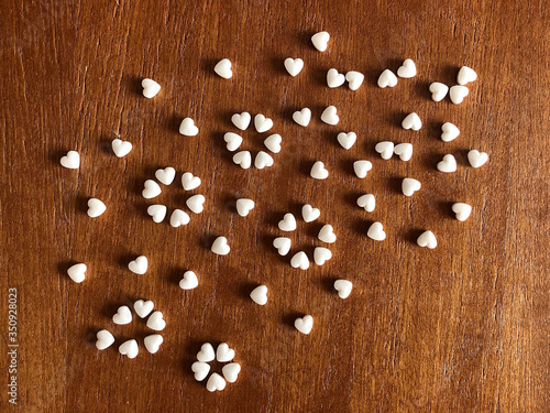 White pills in the shape of a heart scattered on a wooden background. Coronavirus concept.