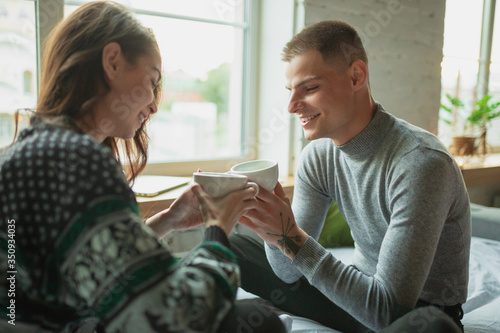 Drink tea, calm. Quarantine lockdown, stay home concept - young beautiful caucasian couple enjoying new lifestyle during coronavirus worldwide health emergency. Happiness, togetherness, healthcare.