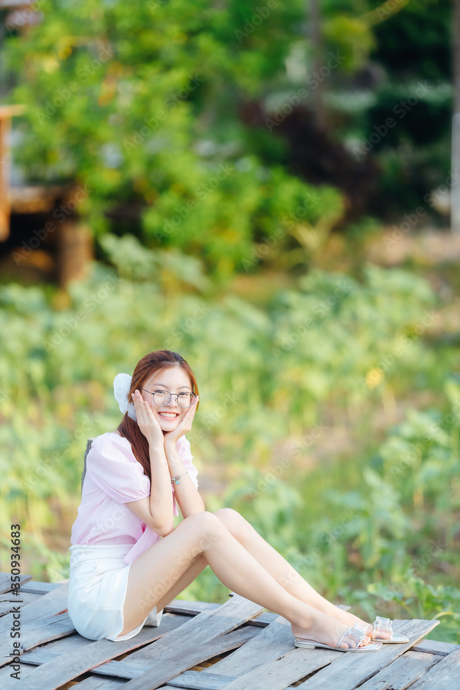Asian cute girl with glasses wear pink shirt and white pants sitting on wooden bridge in garden at home. Asian cute girl with glasses wear pink shirt and white pants sitting on wooden bridge in garden at home.