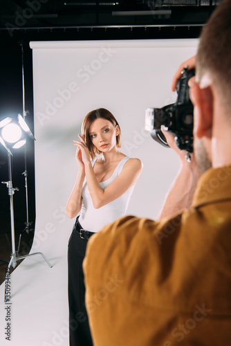 Selective focus of photographer taking photo of beautiful model in photo studio