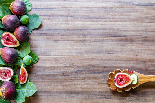 Top view of figs, green leaves on rustic wooden background