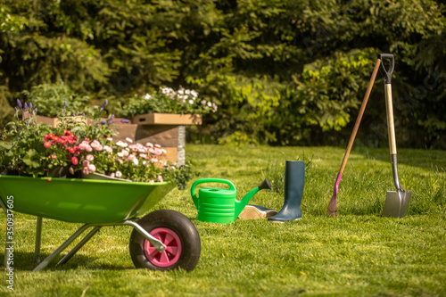 Urban garden in boxes. Wheelbarrow with gardening tools in the garden. Rakes, shovel, pitchfork, watering can. Beautiful background for the gardening concept
