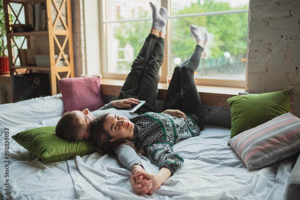 Obraz premium Lying down, lovely. Quarantine lockdown, stay home concept - young beautiful caucasian couple enjoying new lifestyle during coronavirus worldwide health emergency. Happiness, togetherness, healthcare.