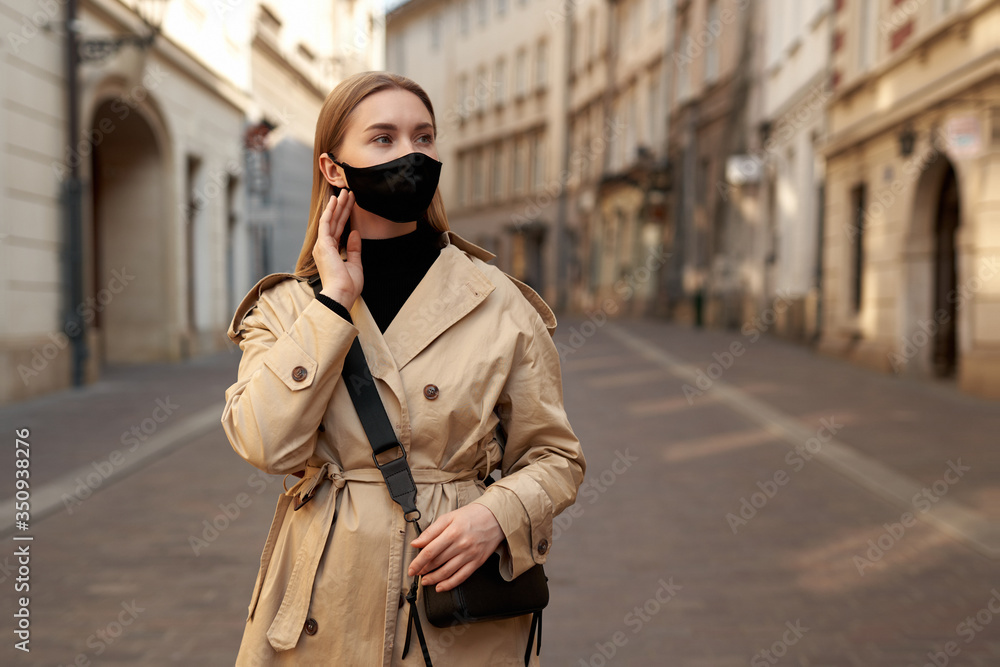 Fototapeta premium Woman wearing trendy fashion outfit during quarantine of coronavirus outbreak. Model dressed protective stylish handmade face mask. Tourist walkin on empty street. Woman with fashion protective mask.