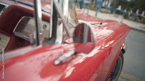 Details of red retro car on a blurred city background. Action. Close up of round rear view mirror of the old fashioned polished shiny red vehicle.