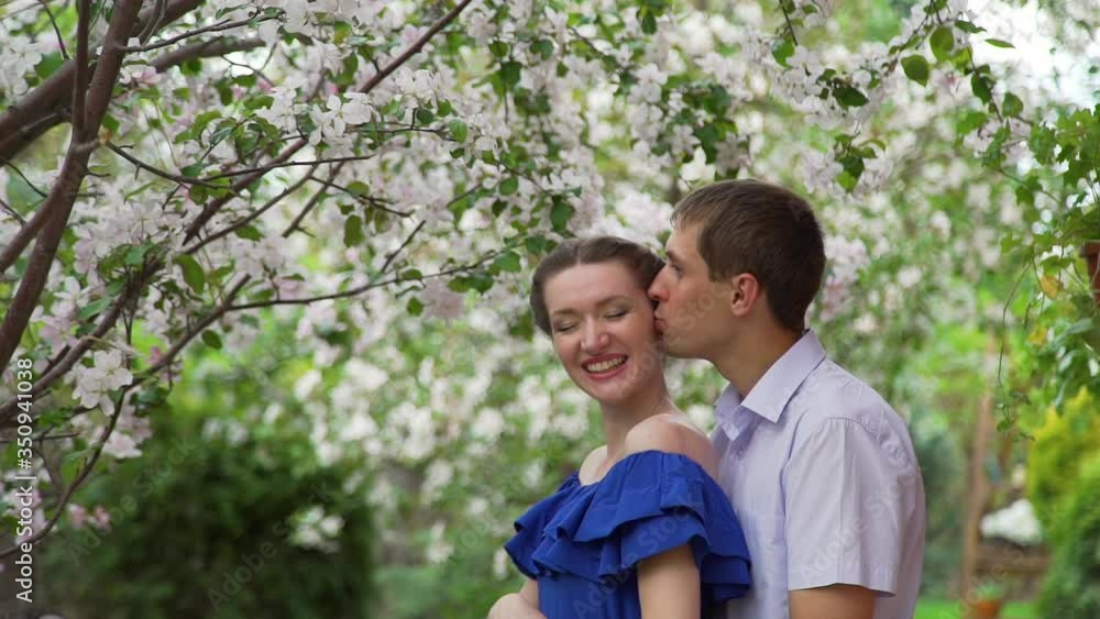 Young Man Kissing his Girlfriend in a Spring Park. Loving Couple Embracing in a Blooming Apple Garden. Love, Dating, Romantic Relationships and Spring Time Concept Young Man Kissing his Girlfriend in a Spring Park. Loving Couple Embracing in a Blooming Apple Garden. Love, Dating, Romantic Relationships and Spring Time Concept