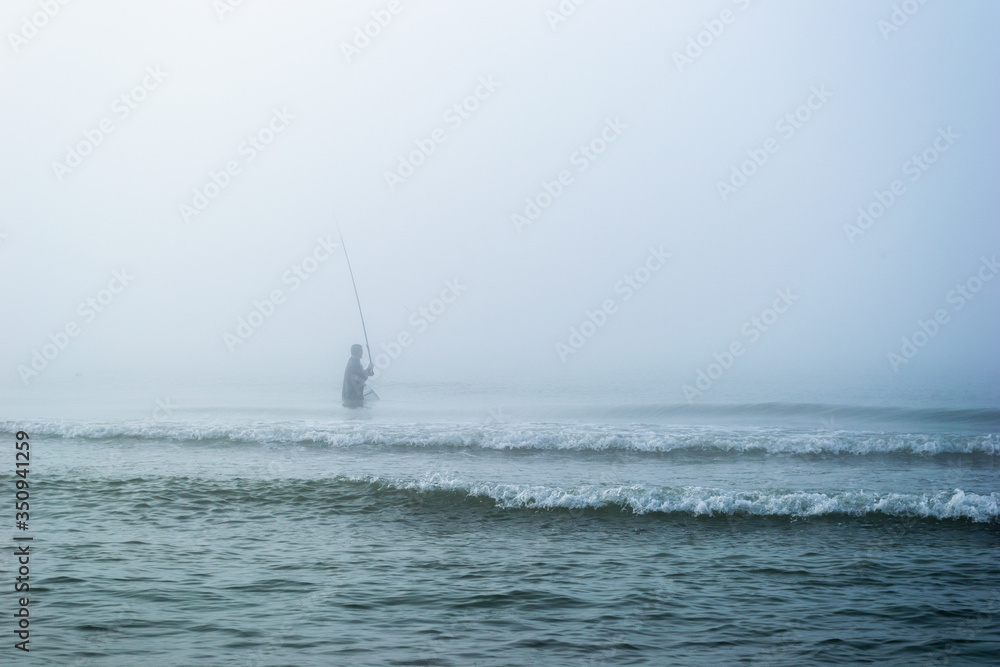 Fisherman fishing on the seashore in the fog