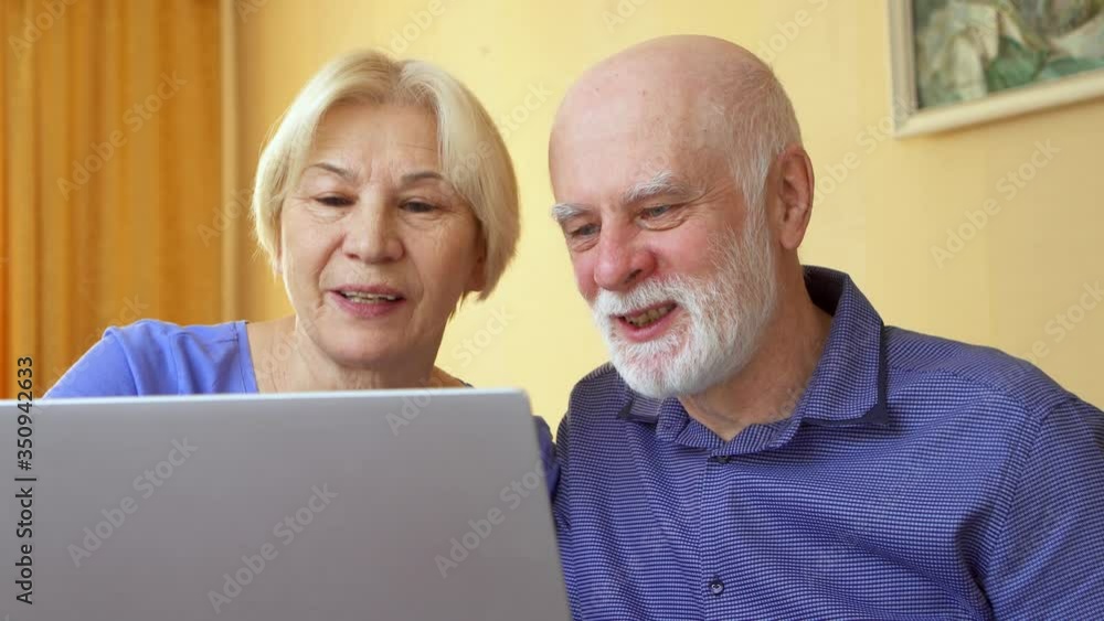 Senior couple working from remote home office on laptop. Retired family staying home and using computer to have video chat with their children. Active modern lifestyle on retirement Senior couple working from remote home office on laptop. Retired family staying home and using computer to have video chat with their children. Active modern lifestyle on retirement