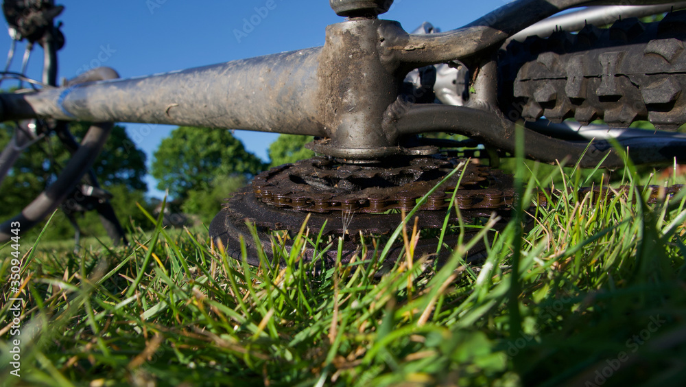 Underside of muddy used bike lying on grass against blue sky