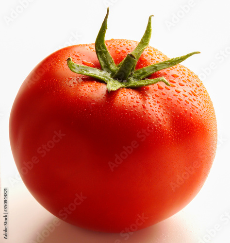 Whole ripe tomato with stalk and water droplets against white background