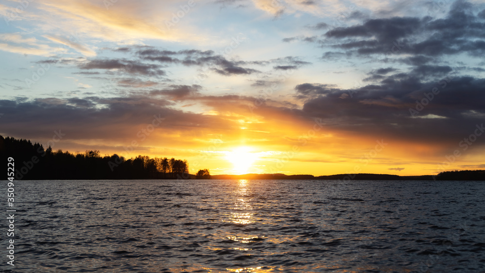 Midnight sun with water reflection at beautiful lake in finland, scandinavia, europe. Dramatic sunset over lake, waves and passing clouds. Holidays and tarvel destination.