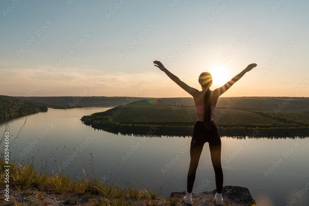 Silhouette of a sporty young woman standing on a ridge, enjoying the sunset over a river valley Silhouette of a sporty young woman standing on a ridge, enjoying the sunset over a river valley