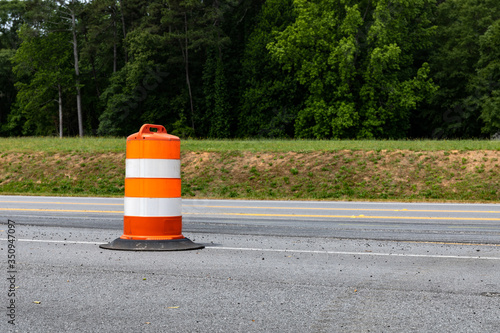 Rural road with orange and white striped plastic traffic barrel, road construction, copy space, horizontal aspect