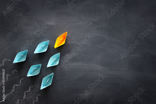 Leadership banner concept with paper boat on blackboard background. One leader ship leads others