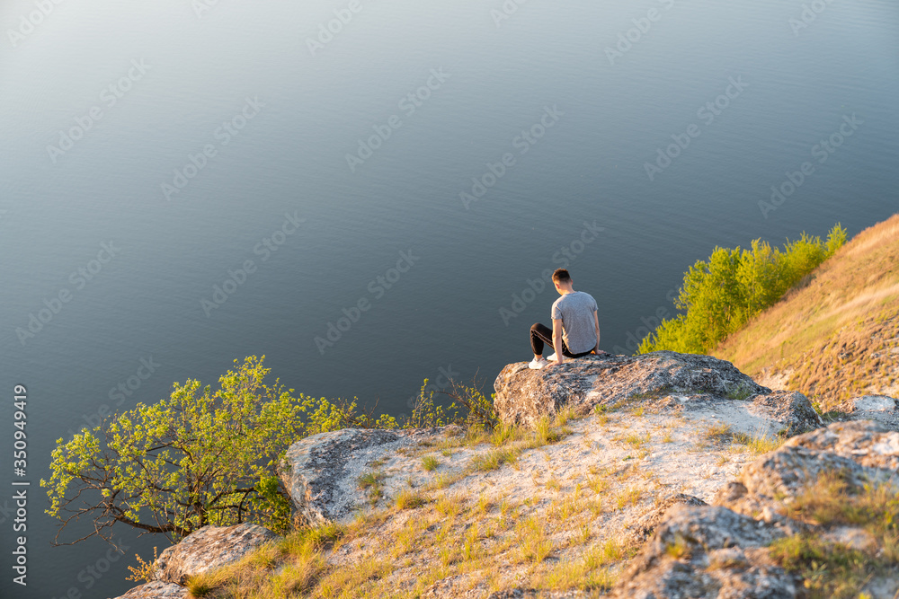 Young man in casual clothes sitting back to the camera on the rock