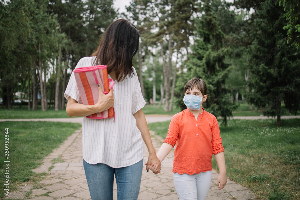 Family walking in park while wearing masks against coronavirus. Young woman and child holding their hands and wearing antivirus masks while walking in park.