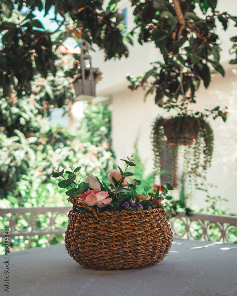 Wicker basket filled with flowers on table. Basket with artificial flowers on vernada.