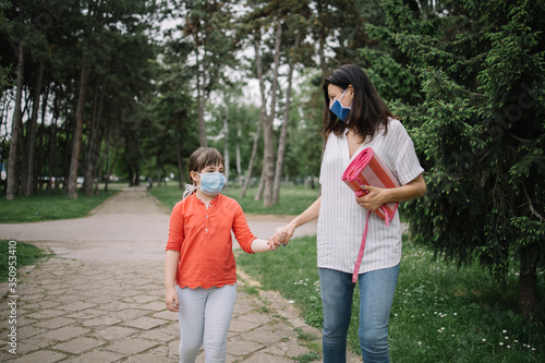 Mother and daughter walking in park while holding their hands. Woman and child holding their hands while walking in park and wearing antivirus masks. © Synergic Works OÜ