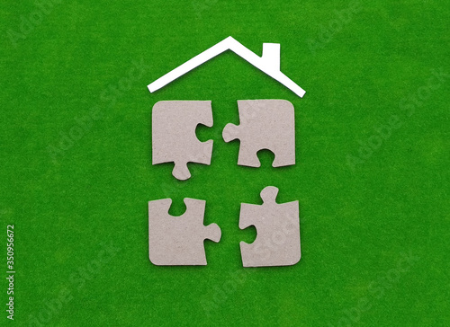Under the roof of the house, four pieces of puzzles on a green background. The share of the property, the sale of the property.