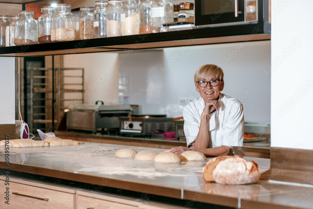 Fototapeta premium Senior female baker preparing dough for bread in modern manufacturing.