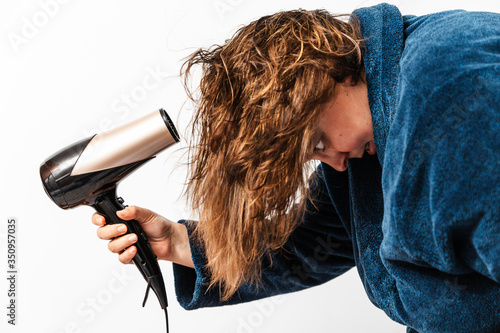 es una mujer.  de 40 años y sobrepeso caucásica con pelo moreno lleva un secador en la mano para secar su cabello mojado. lleva un albornoz azul. photo