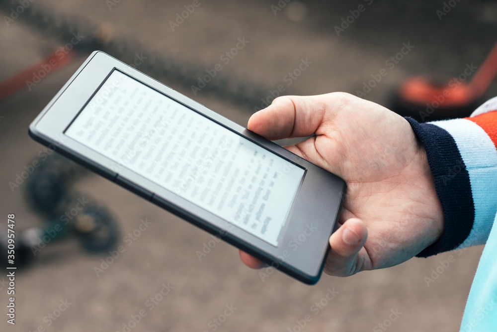 Male hand with modern gray electronic book. Reading books everywhere with a pocket reader or tablet. Selective focus. Closeup view. Blurred background
