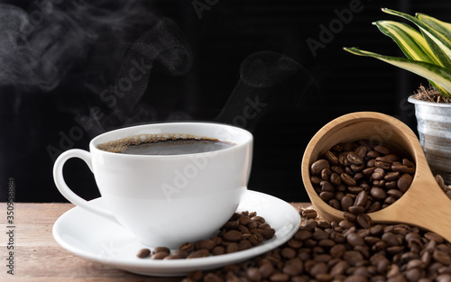 Steam coffee cup with roasted beans and flower pot on wood background in morning sunlight