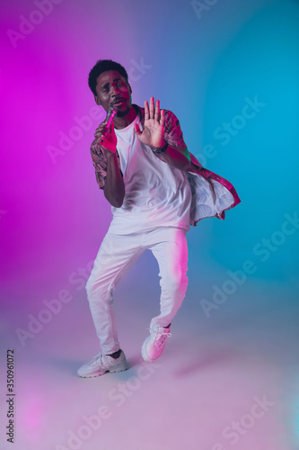 African-american male singer portrait isolated on gradient studio background in neon light. Beautiful male model with microphone. Concept of human emotions, facial expression, ad, music, art.