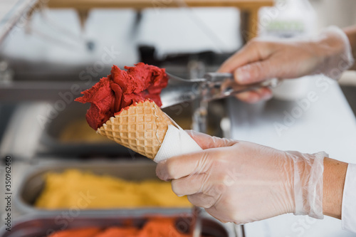 Ice cream in a waffle cup. Strawberry ice cream. Ice cream maker makes ice cream in the summer. The hands of an ice cream seller. 