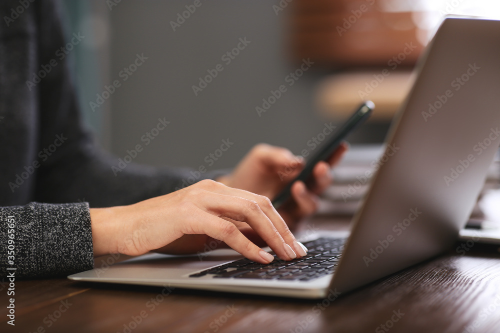 Woman with mobile phone working on modern laptop at table, closeup Woman with mobile phone working on modern laptop at table, closeup