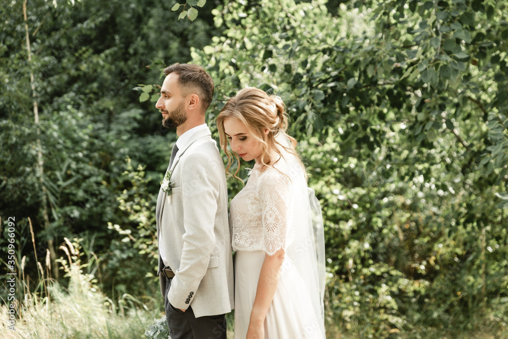 Bride and groom on their wedding day, walking outdoors in spring nature. Just married, happy newlywed woman and man embracing in a green park. Loving wedding couple outdoors. Bride and groom