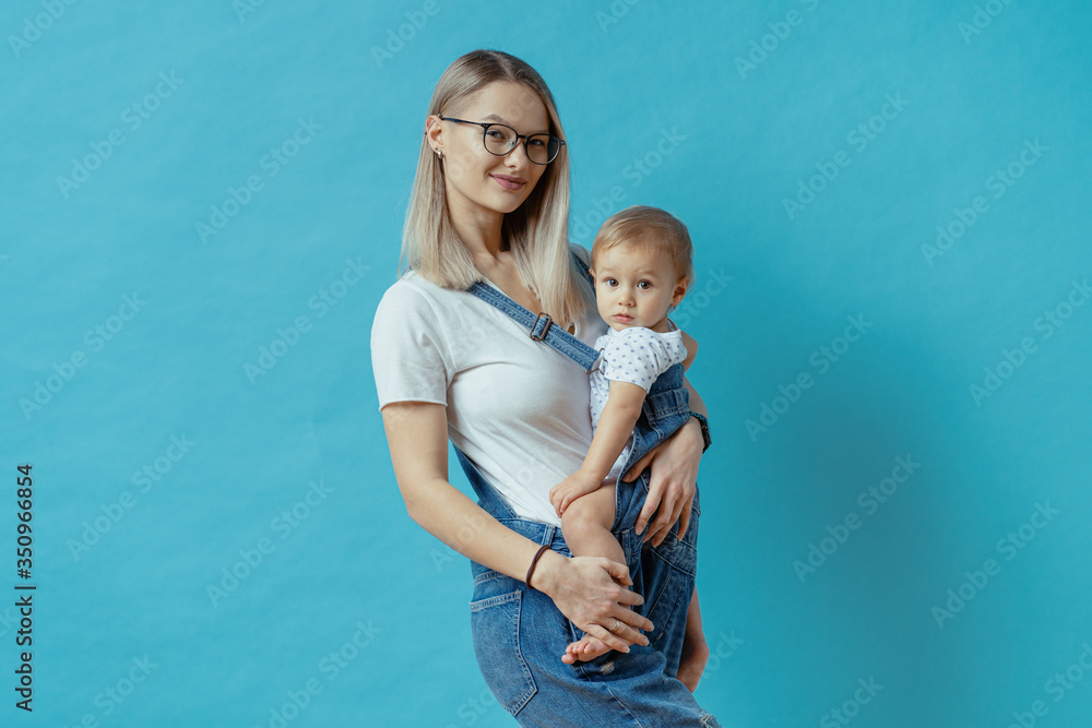 Cheerful young mom posing with her one year kid on blue background