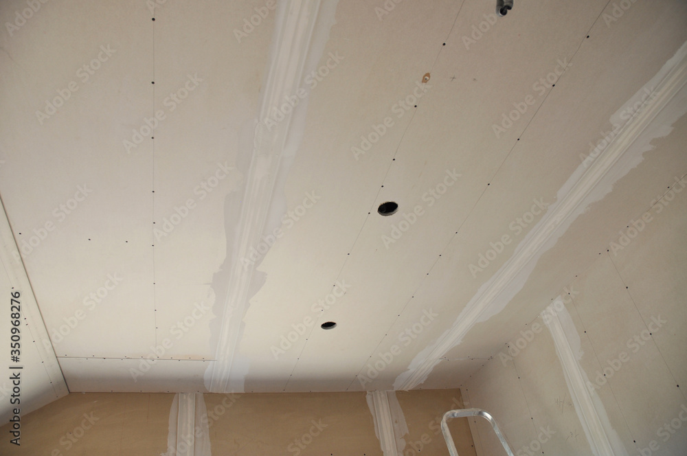 Closeup on plastering, skim coating, finishing a drywall ceiling and walls with cut holes for