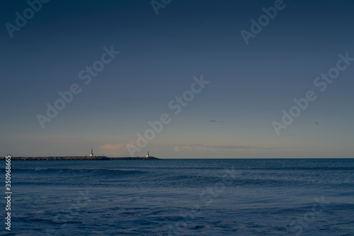 Beach with breakwater and lighthouse visible and calm waves. © herme