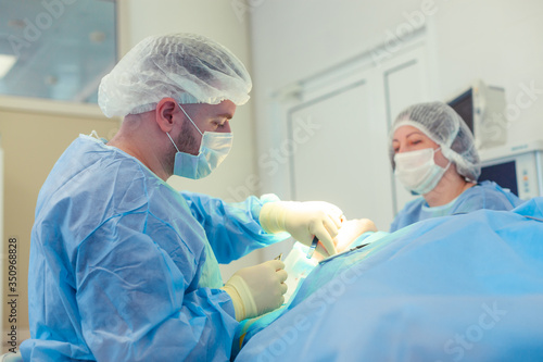 Male surgeon performs surgical procedures in the operating room, while his assistant monitors the patient condition