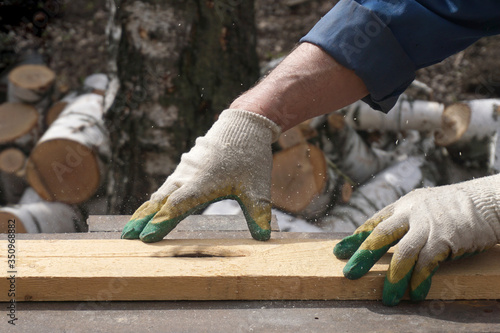 Obraz na plátně A circular saw cuts a board held by a gloved hands of a joiner.