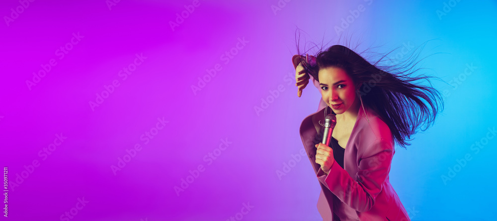 Caucasian female singer portrait isolated on gradient studio background in neon light. Beautiful female model in pink wear with microphone. Concept of human emotions, facial expression, ad, music, art Caucasian female singer portrait isolated on gradient studio background in neon light. Beautiful female model in pink wear with microphone. Concept of human emotions, facial expression, ad, music, art